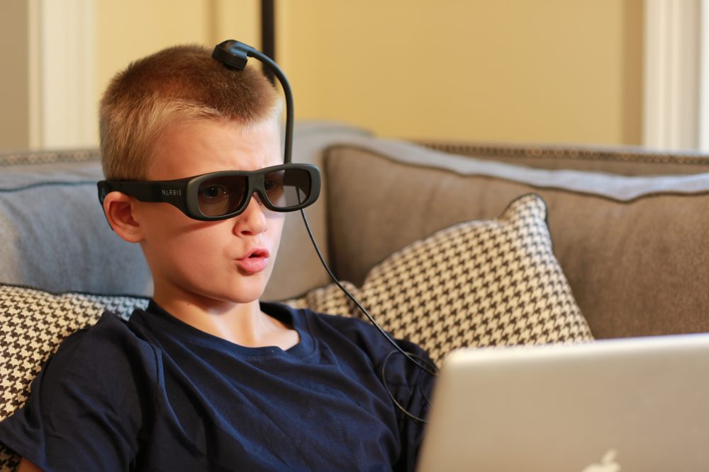 A boy wearing Narbis smart glasses while working on a laptop at home